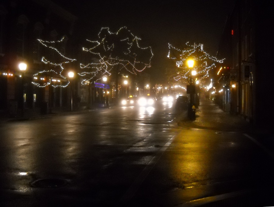 cold, foggy city street at night with christmas lights in trees