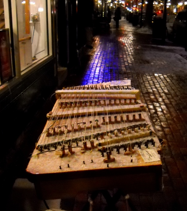 snow-coverd dulcimer at night with many colered city lights reflecting off wet brick sidewalk 