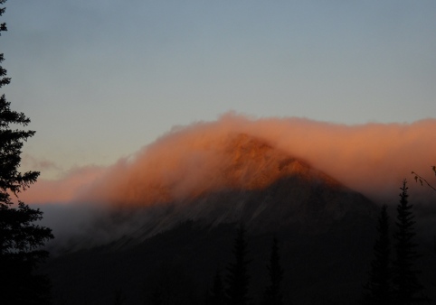 clouds flowing over a mountain like a wave, lit by the sunrise