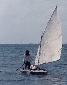 brian sailing his small open sailing kayak Horse, standing in white tropical pajamas, with his white wolf-dog on deck