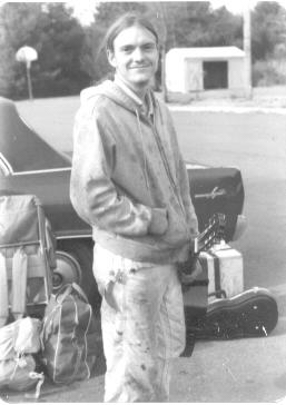 brian in 1981 in a coffeehouse parking lot with guitar in hand and reel to reel in a packing box in background